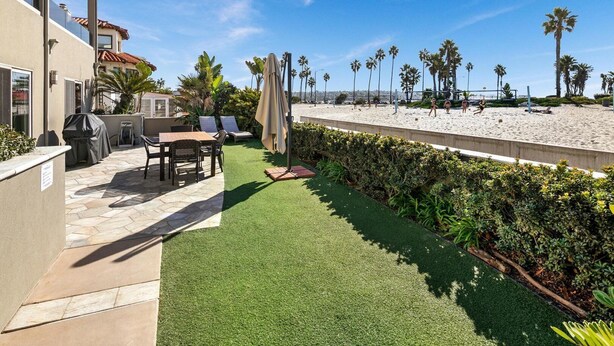 A patio with a table and chairs, a grill, and a view of the beach with palm trees. - Three Bedroom on the Ocean Front! (San Diego)