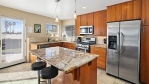 A modern kitchen with wooden cabinets, stainless steel appliances, a granite countertop, and a bar stool. - Three Bedroom on the Ocean Front! (San Diego)