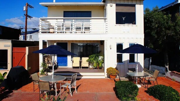 A modern two-story house with a patio area featuring outdoor seating and umbrellas.
