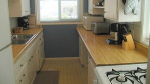 A compact kitchen with white cabinets, a gas stove, a microwave, and a window with blinds.