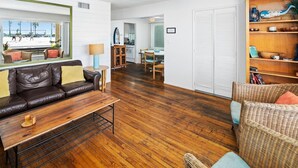 A modern living room with a leather sofa, a wooden coffee table, and a wicker chair. A kitchen area is visible in the background with a dining table and chairs. - Cute and cozy one-bedroom unit in South Mission (San Diego)