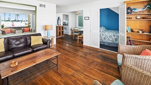 A modern living room with a leather sofa, wooden coffee table, and a wicker chair. A dining area with a table and chairs is visible in the background. - Cute and cozy one-bedroom unit in South Mission (San Diego)