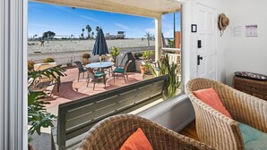 A balcony with wicker furniture, a table, and chairs, overlooking a beach with umbrellas and plants. - Cute and cozy one-bedroom unit in South Mission (San Diego)