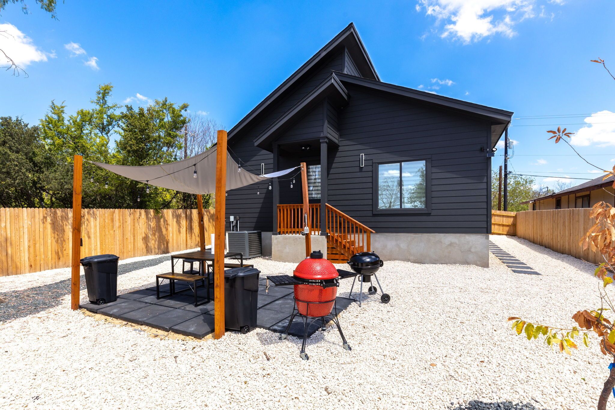 Une maison moderne dotée d’un patio couvert, d’un barbecue extérieur et d’une clôture en bois.