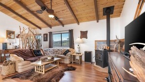 A cozy living room with a fireplace, wooden ceiling beams, and a sofa set. - No longer available for short term rental due to county restrictions (Captain Cook)