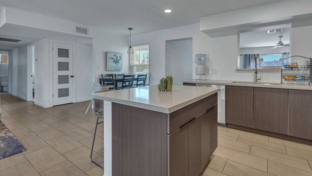 A modern kitchen with a central island, wooden cabinets, and a dining area with a table and chairs. - Urban Desert Home (Phoenix)