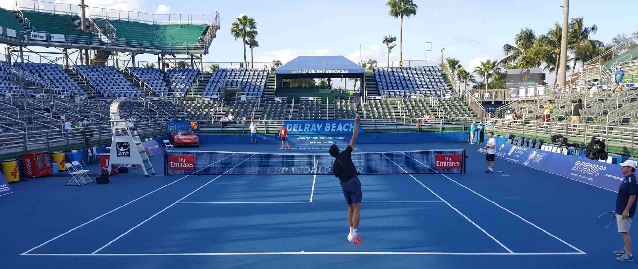 A tennis court with a net, advertising banners, and empty spectator stands.