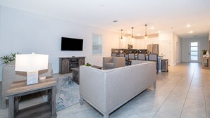 A modern living room with a sectional sofa, a TV, and a kitchen in the background. - 9056SH: Meticulous 8 bed in The Retreat at ChampionsGate with No rear neighbors (Davenport)