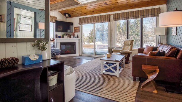 A cozy living room with a fireplace, comfortable seating, and large windows offering a view of the outdoors. - Crisp Cabin: Waterfront, 2 Kayaks, AC + Walk Downtown (Rangeley)