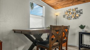 Un coin repas avec une table et des chaises en bois, une fenêtre avec des stores, un luminaire fixé au mur et un élément décoratif mural.