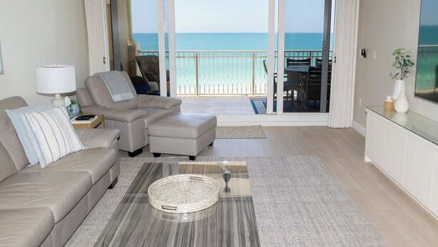 A living room with a sofa, armchair, and ottoman, a coffee table, and a view of the ocean through large sliding doors. - Luxury Direct Beachfront 3-bedroom Pet-Friendly Gated Condo in Redington Shores (Redington Shores)