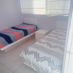 A small, single-room with two beds, a white tiled floor, and a window with blinds. - Beautiful beach/lake house (San Antonio)