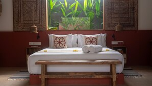 A bedroom with a large bed, a wooden bench, a window with plants, and patterned walls. - Lasai Villas (Gili Air)