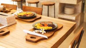 A wooden dining table with a breakfast plate containing eggs, beans, and tomatoes. There are wooden chairs and a woven basket on the table. - Lasai Villas (Gili Air)
