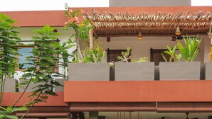 A swimming pool with a person sitting on the edge, another person holding a drink, and a house with a red roof and plants in the background. - Lasai Villas (Gili Air)