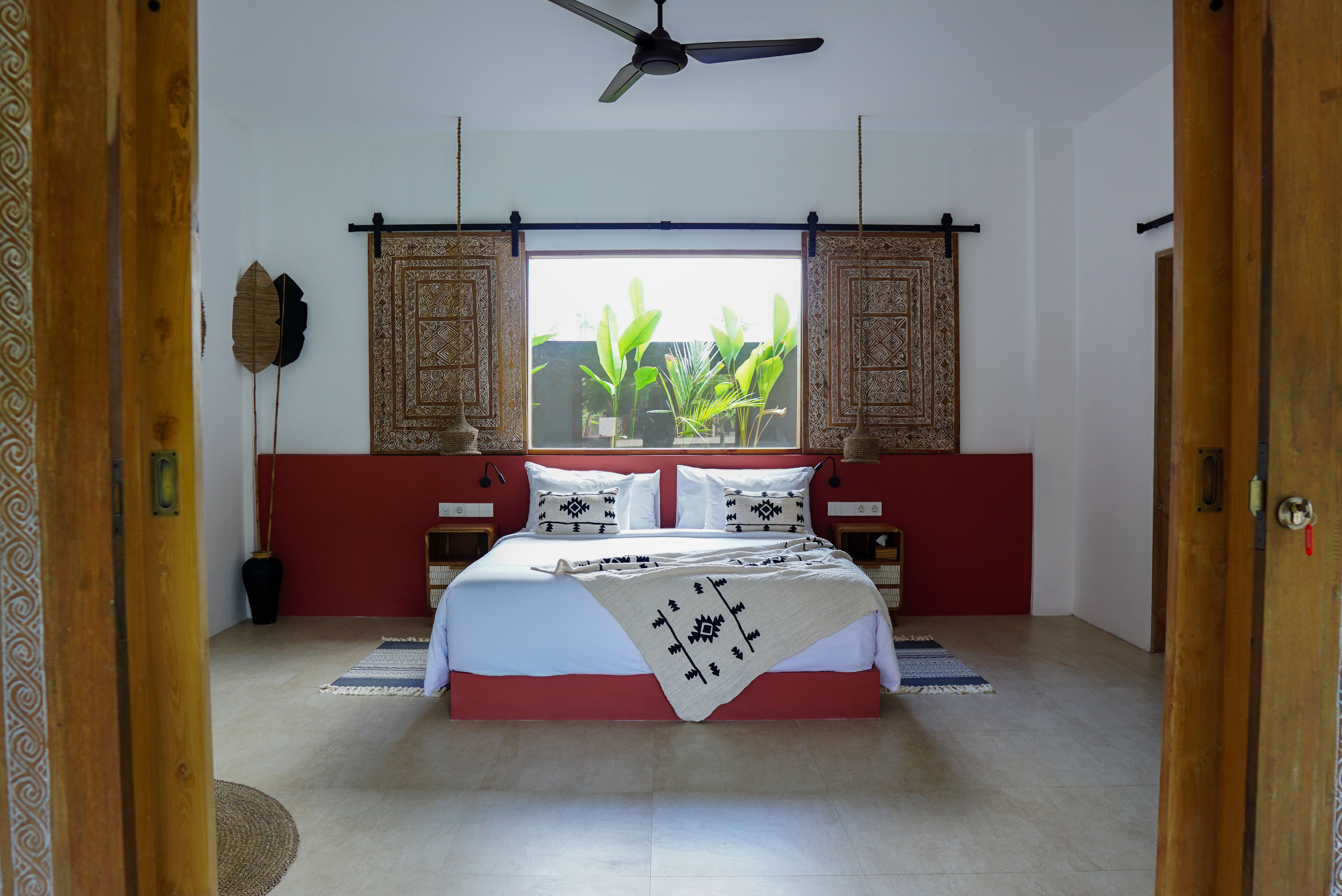 A bedroom with a large bed, a ceiling fan, and a window with a view of greenery.