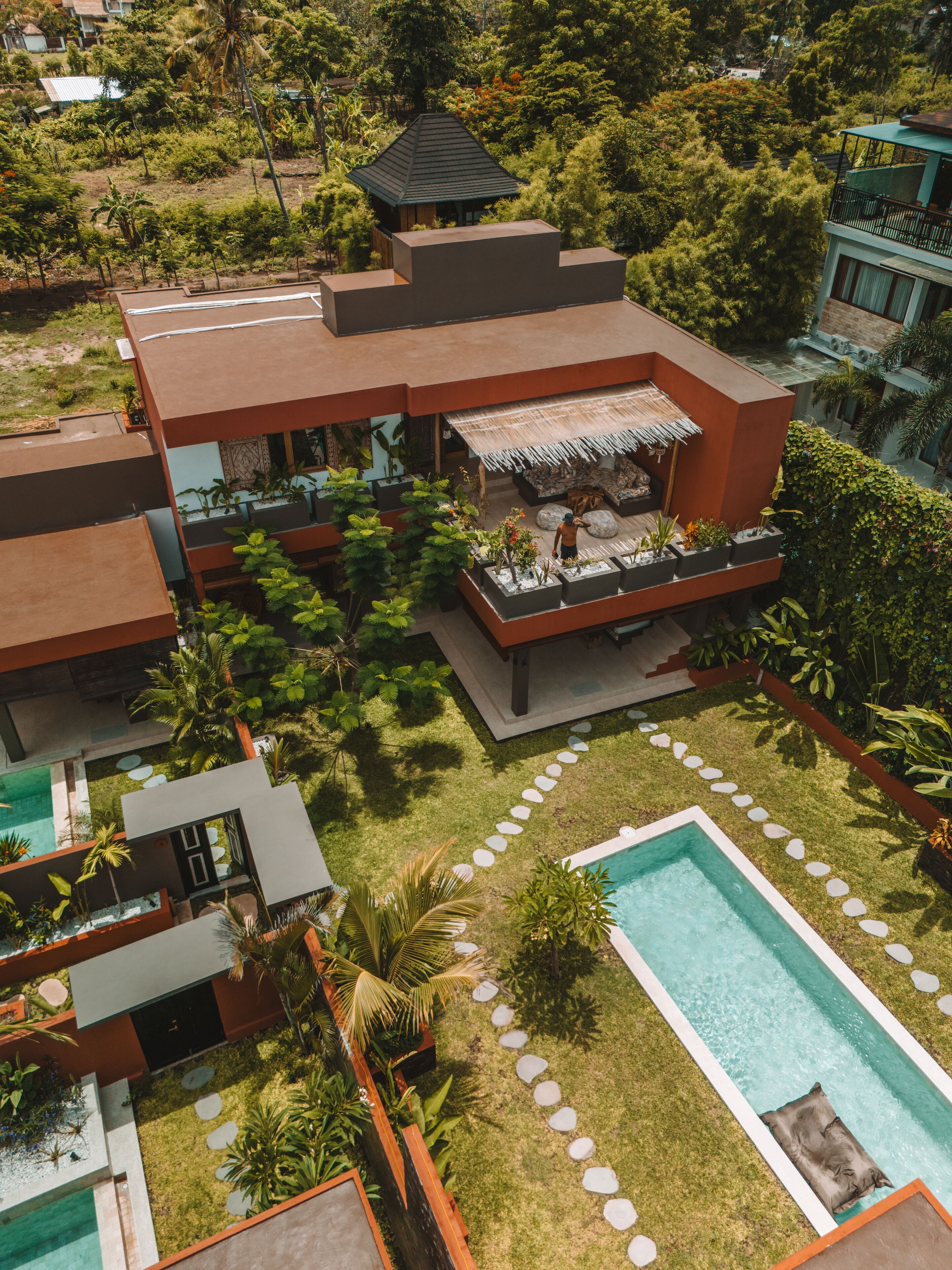 A modern house with a pool, surrounded by lush greenery and a thatched-roof outdoor seating area.