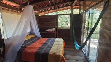 A room with a bed, a bedside table, and a window with a view of trees.