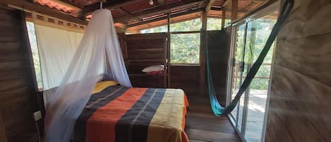 A room with a bed, a bedside table, and a window with a view of trees.