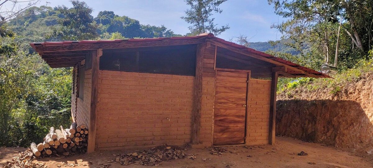 A small wooden structure with a sloped roof, a single door, and a stack of firewood outside.