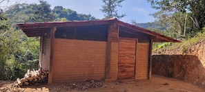 A small wooden structure with a sloped roof, a single door, and a stack of firewood outside.