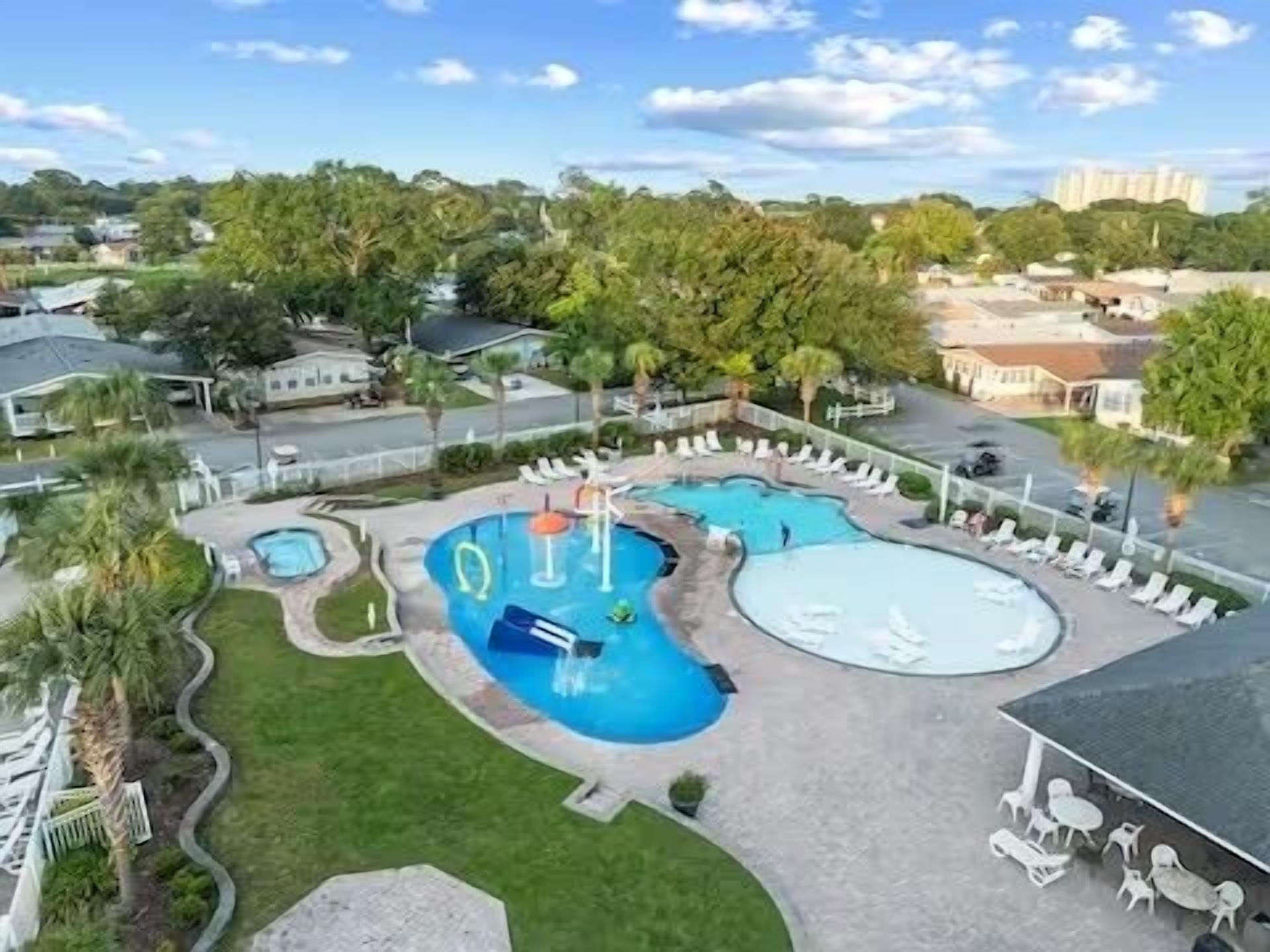 A large outdoor swimming pool with multiple sections and a water slide, surrounded by lounge chairs and a grassy area.