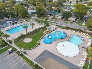 Eine Luftaufnahme eines Resorts mit mehreren Schwimmbecken, Liegebereichen und einem Parkplatz.