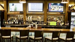 A bar area with multiple TVs, a well-stocked bar, and several bar stools.