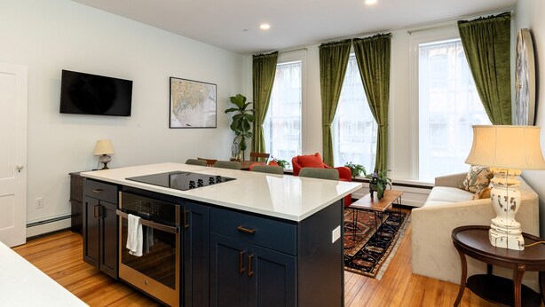 Una cocina moderna con una isla central, horno empotrado y un área de comedor con sofá y mesa.