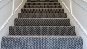 Una escalera con escalones alfombrados, paredes blancas y una lámpara en la parte superior.