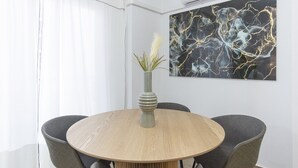 Una mesa de comedor redonda con tapa de madera y un florero con una planta. Hay dos sillas alrededor de la mesa. Un cuadro abstracto grande está en la pared sobre la mesa.