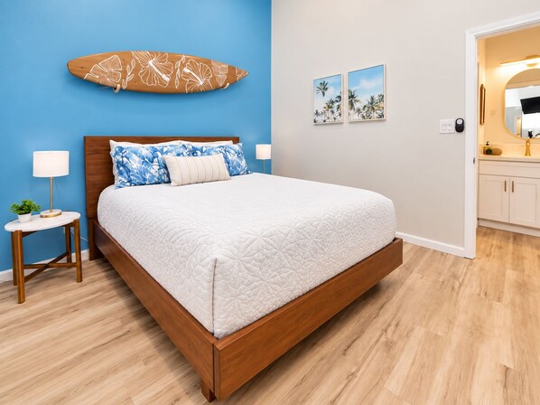 A bedroom with a wooden bed, a blue wall, a small bedside table with a lamp, and a nightstand with a plant.