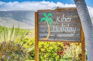 A wooden sign with a palm tree and the text 'Kihei Holiday' and '483 South Kihei Rd.'