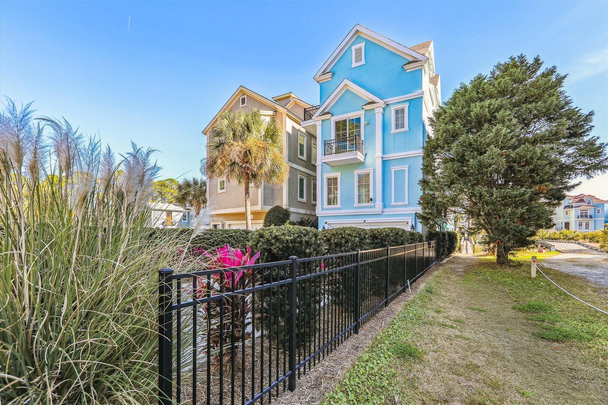 A two-story building with a blue facade and white trim, surrounded by greenery and a black metal fence.