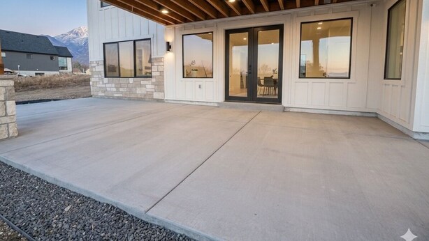 A covered patio area with a concrete floor, large windows, and a view of a mountain. - Brand new apartment, sleeps 10, IDEAL location in Utah county. High end finishes (Lindon)