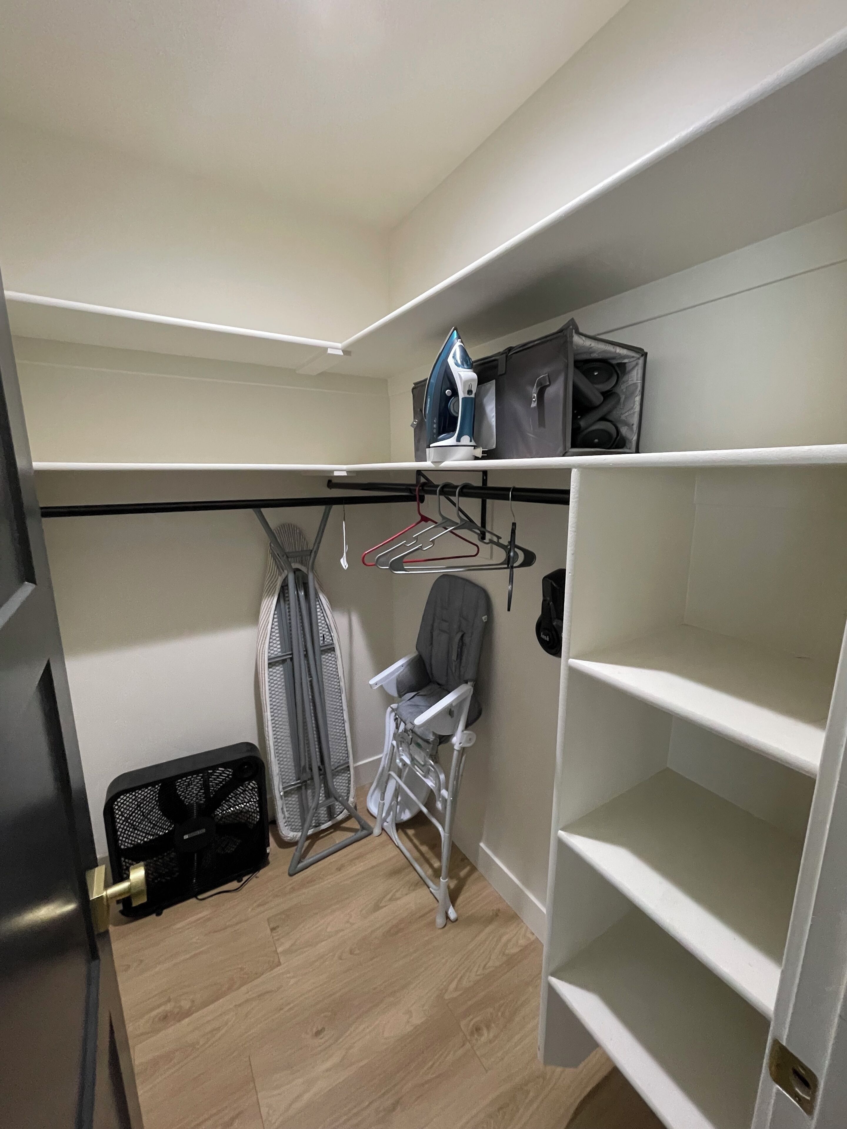 A compact room with a built-in wardrobe, a small ironing station, and a chair.