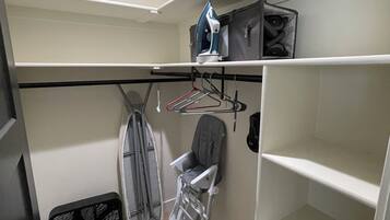 Una habitación compacta con armario empotrado, una plancha pequeña y una silla.