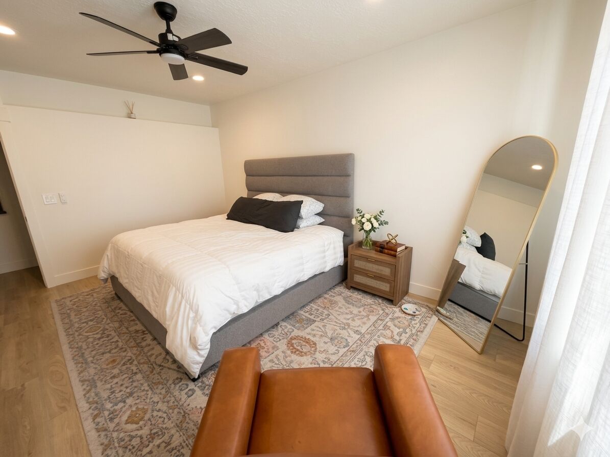Una camera da letto con un letto, un comodino, uno specchio, una ventola a soffitto e una sedia.