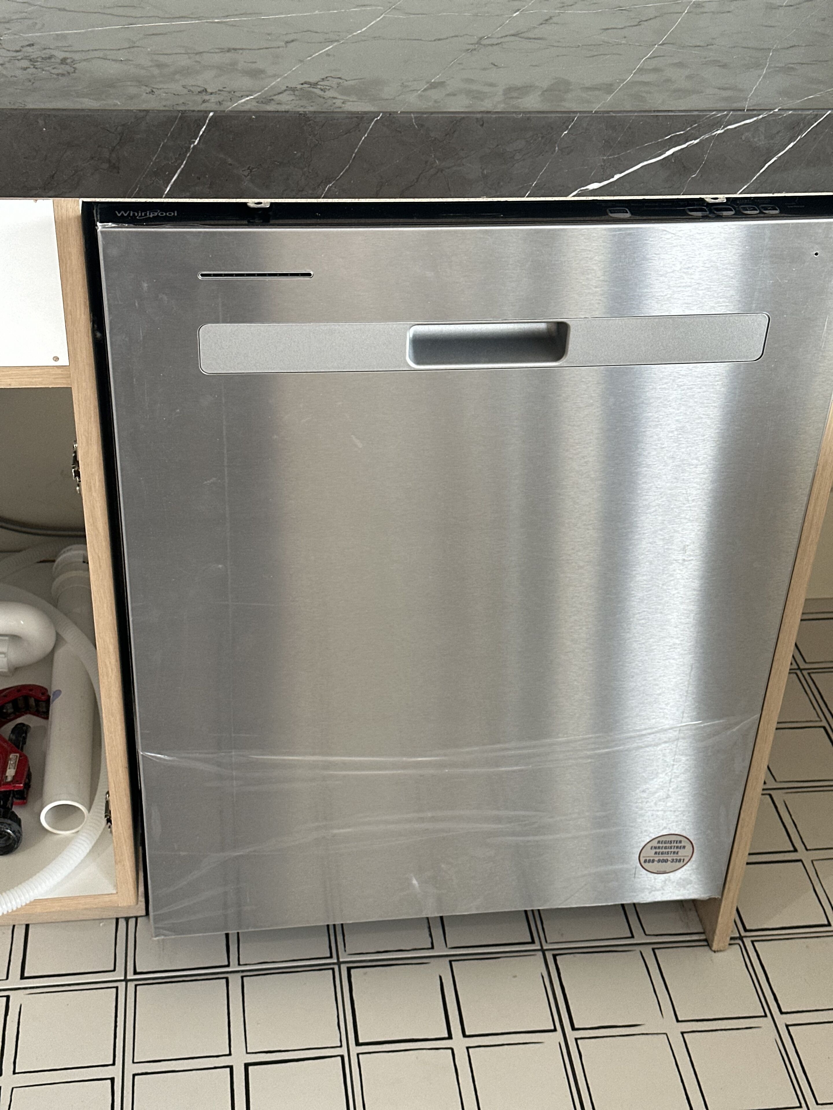 A stainless steel dishwasher in a kitchen with a tiled floor and a black countertop.