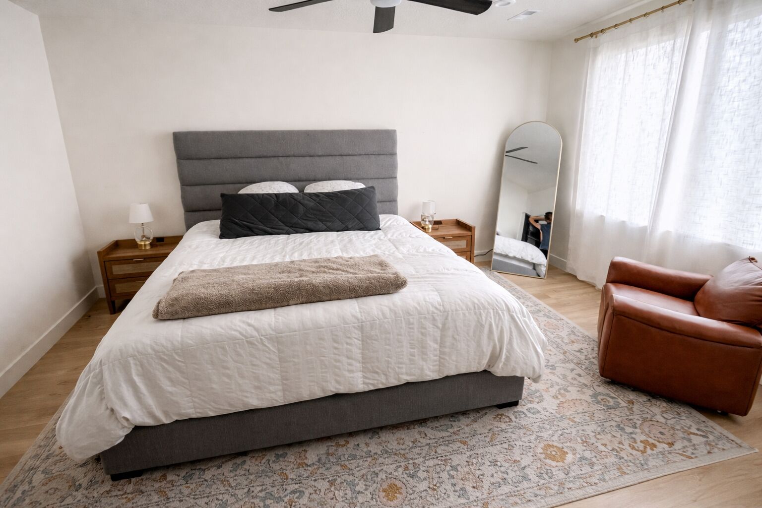Un dormitorio con cama, mesitas de noche, un espejo, una silla y una alfombra estampada.