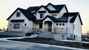 A two-story house with a stone foundation, multiple gabled roofs, and a front porch. - Brand new apartment, sleeps 10, IDEAL location in Utah county. High end finishes (Lindon)
