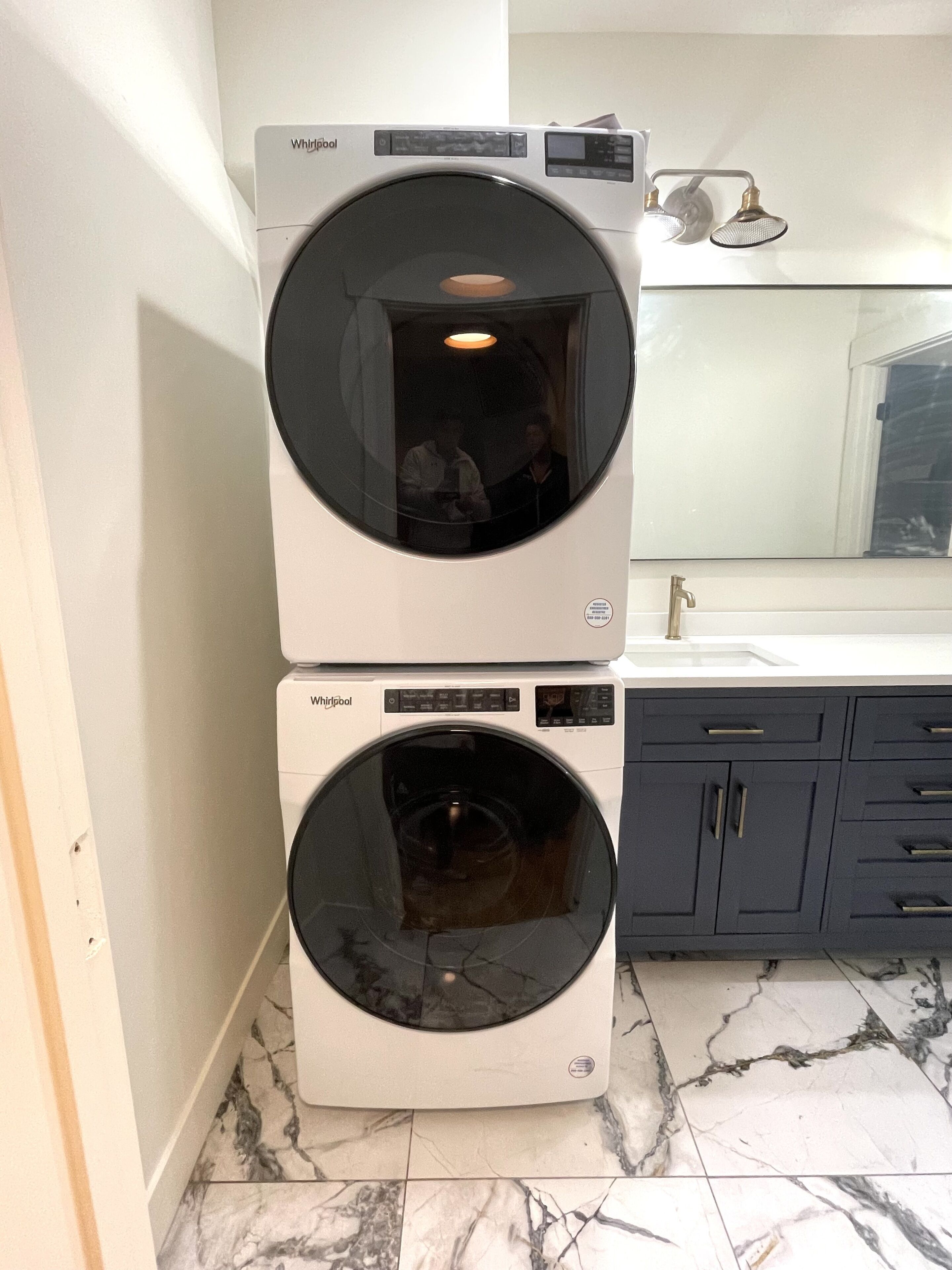 Dos lavadoras Whirlpool apiladas en un baño con un lavamanos blanco y armarios oscuros.