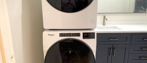 Dos lavadoras Whirlpool apiladas en un baño con un lavamanos blanco y armarios oscuros.