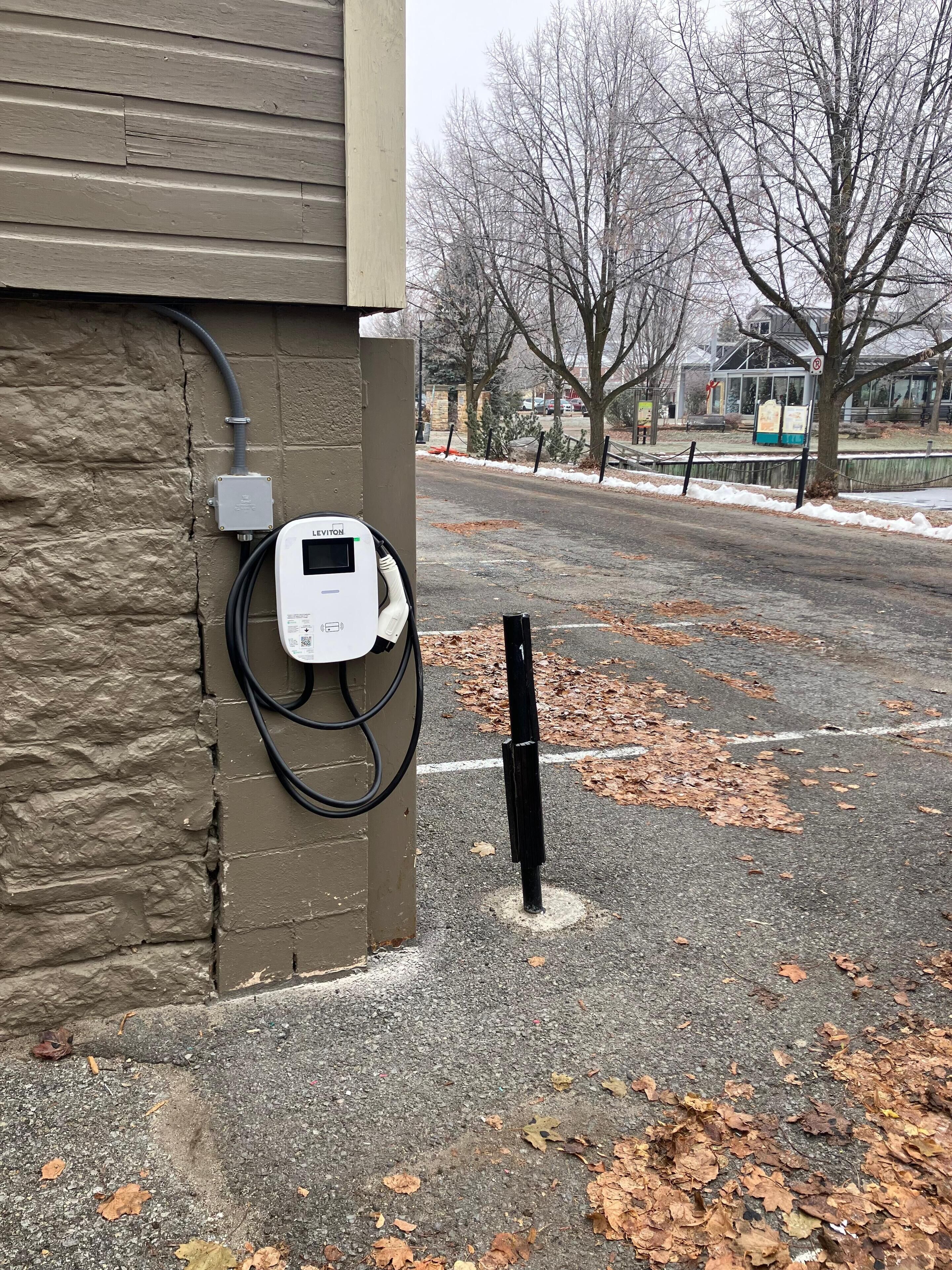 Un espace de stationnement équipé d’une borne de recharge, un mur en pierre et un sol recouvert de feuilles.