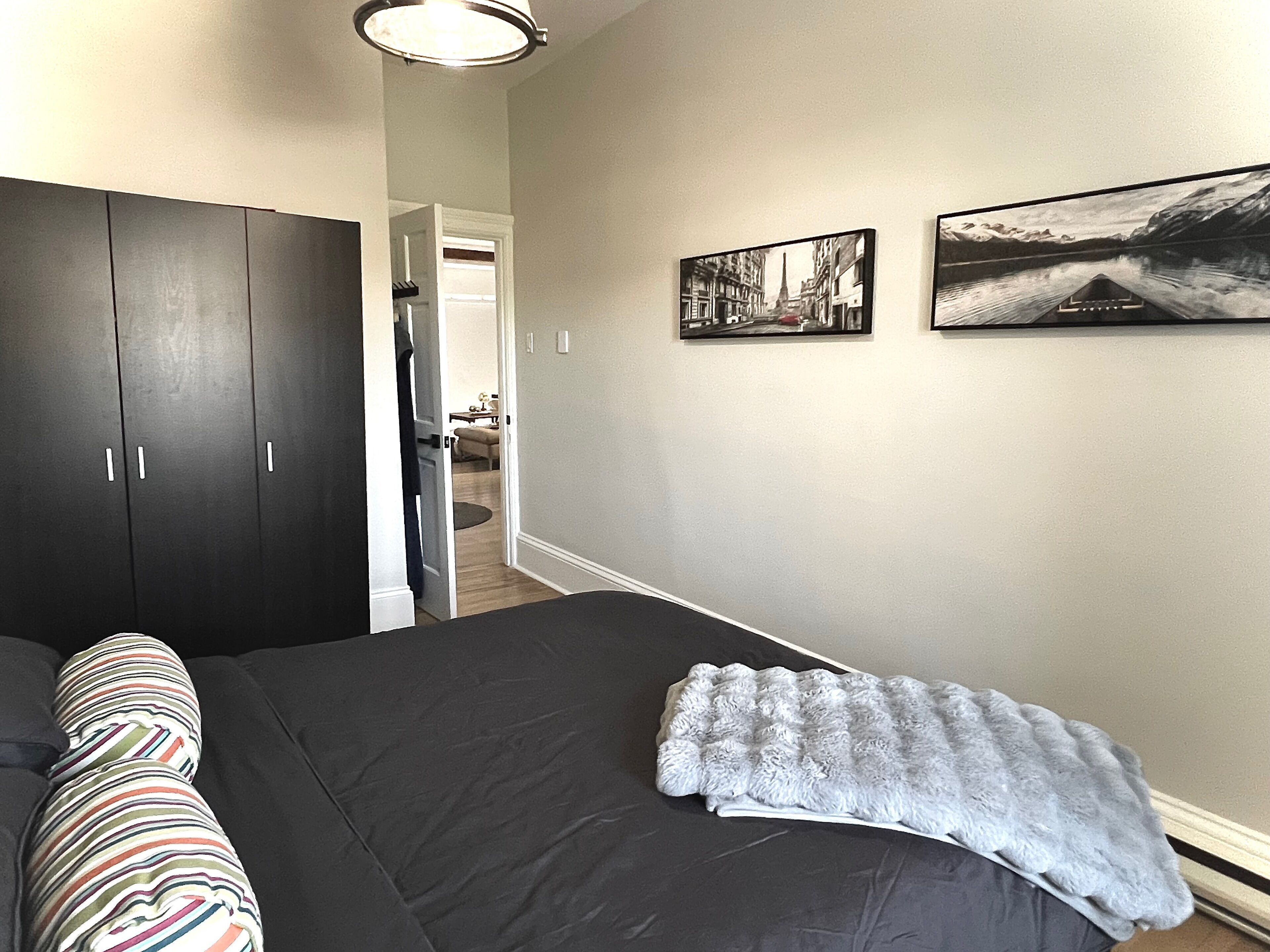 Une chambre à coucher avec un grand lit, une armoire sombre et deux tableaux encadrés accrochés au mur.