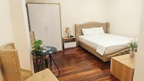 Ein kleiner, gut beleuchteter Raum mit einem Bett, einem Sessel, einem kleinen Tisch und einem Nachttisch.