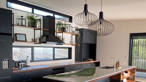 A modern kitchen with a large island, black cabinetry, and a view of the outdoors. - Ahipara Beach Pad (Ahipara)