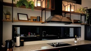 A modern kitchen with a black countertop, a built-in stove, and a large window. - Ahipara Beach Pad (Ahipara)