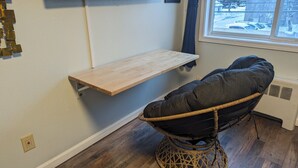 Une pièce avec une étagère en bois, une chaise en osier et une fenêtre donnant sur des voitures garées.