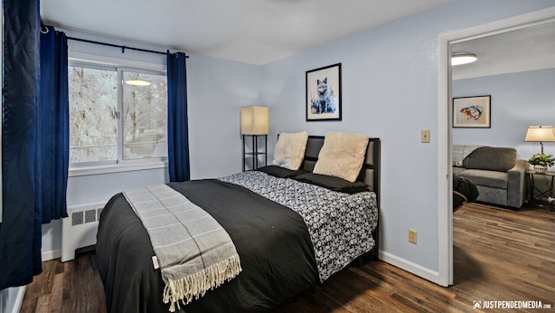 Une chambre avec un grand lit, une fenêtre avec des rideaux, une lampe fixée au mur et un tableau encadré.